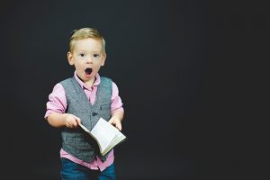 photo of a young boy holding a book and looking shocked