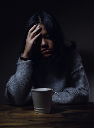Photo of a woman with a cup of coffee and holding her head