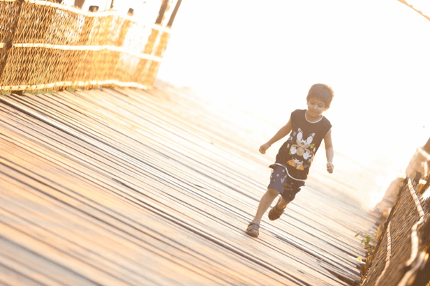 photo of young boy running across a bridge