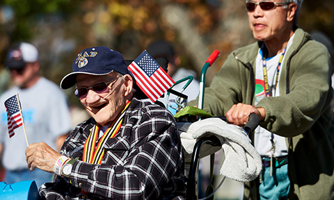 An older veteran in a parade, being escorted by his employee
