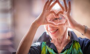 An older woman who is an ACES$ Financial Management client making a heart symbol with her hands