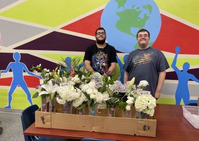two TSC students standing behind bunches of flowers