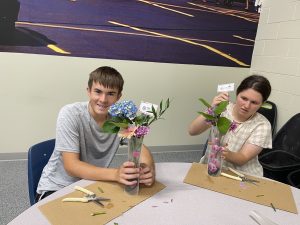 Boy student holding finished flower arrangement next to a girl student working on hers