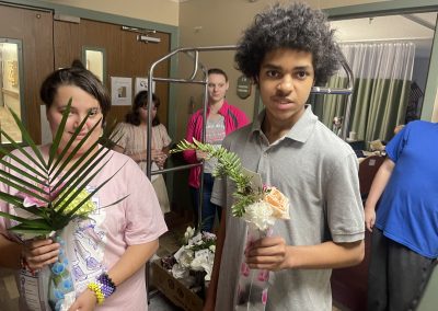 two students holding flower arrangements as they deliver them to an assisted living center