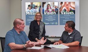 Tim, Kelly and Mike, our executive team, having a discussion in front of our mission, vision and values artwork